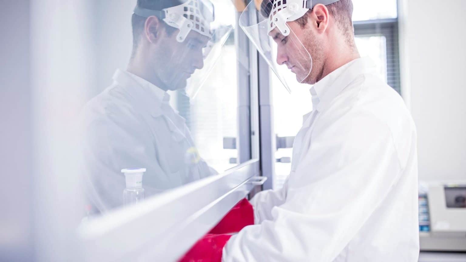 Man wearing personal protective equipment working under a laboratory fume hood.