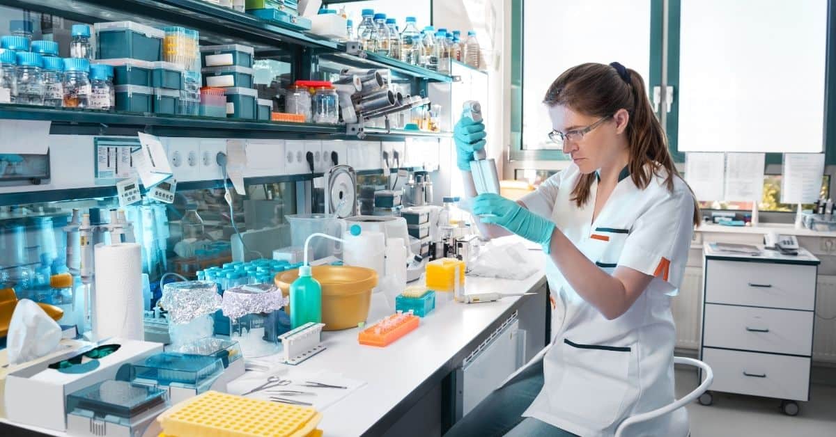 Woman working at a laboratory work surface surrounded by scientific equipment and materials.