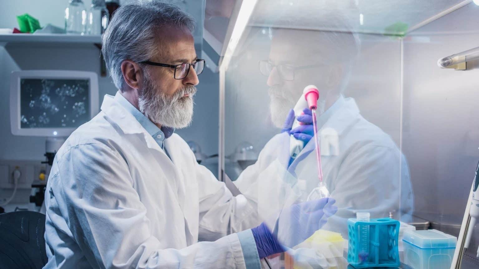 Man working under a laboratory fume hood while handling chemicals.