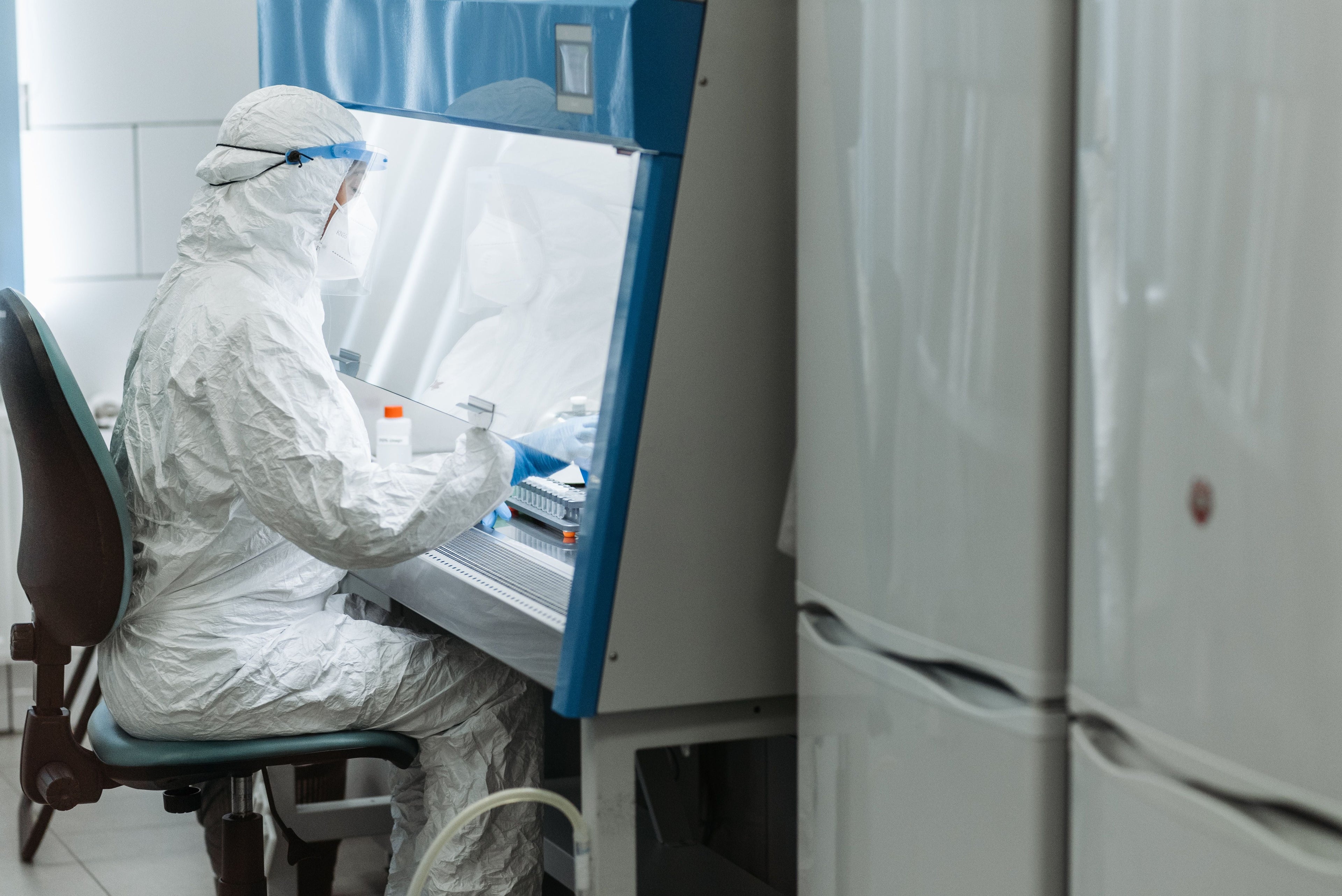 Person in personal protective equipment working under a laboratory fume hood.